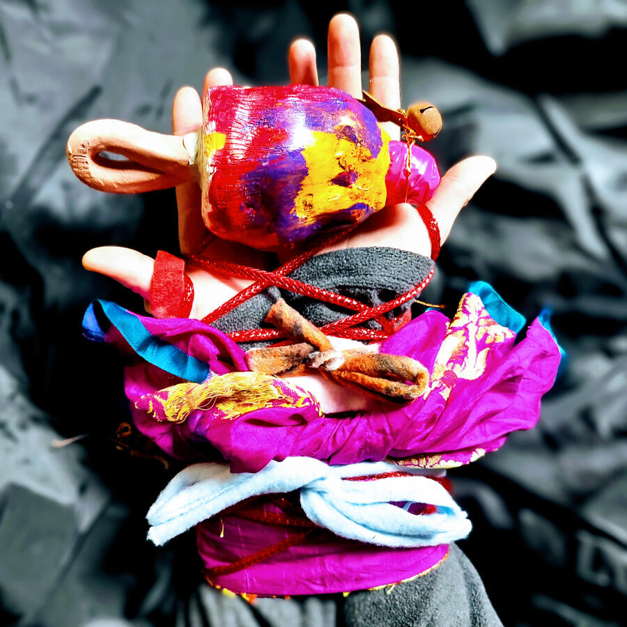 Hands holding a clay bell and bound with colorful scrap cloth and yarn.